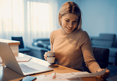 Woman happily looking through financial papers in front of a computer
