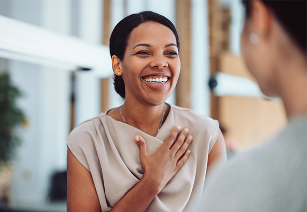 Woman smiling with hand over heart in business setting