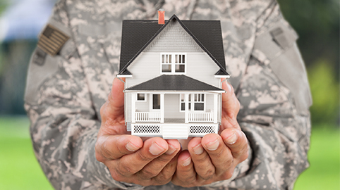Man in military uniform holding model house in hands