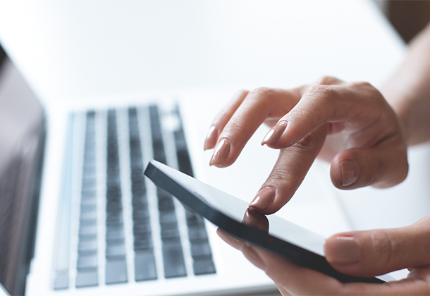 Woman tapping cell phone with laptop in background
